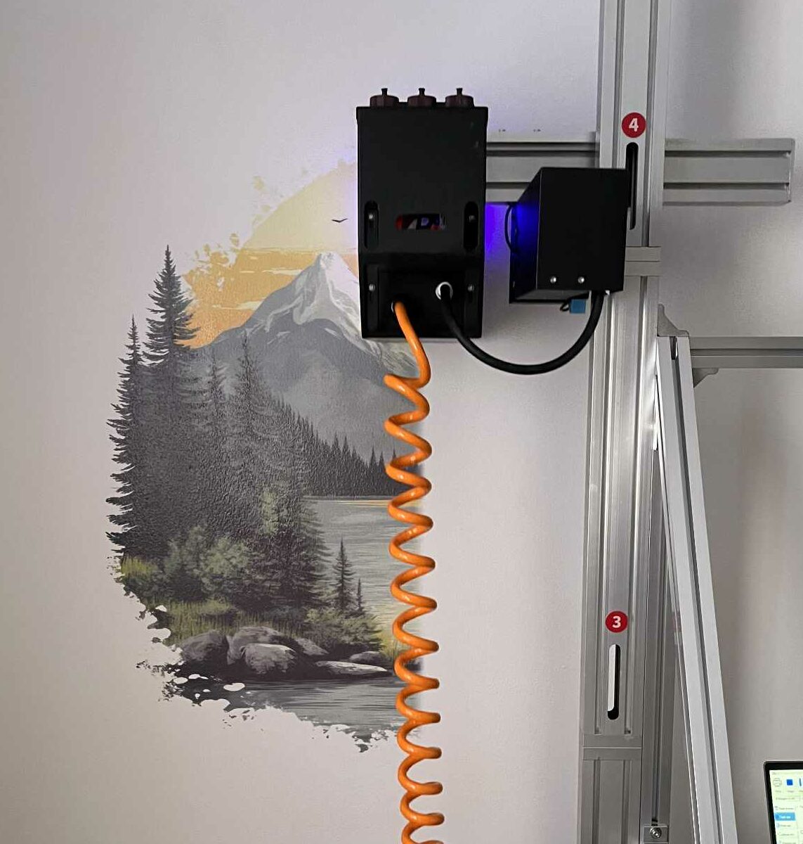 Drukarka ścienna podczas pracy nad tworzeniem muralu z malowniczym krajobrazem górskim, jeziorem i lasem.